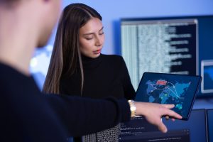 Close-up of a cyber security team working in a Cyber Security Operations Center (SOC). Woman work as Chief Information Security Officer (CISO) and manager pointing on a real time map om tablet.