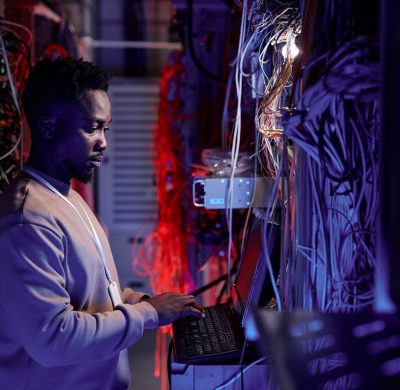 Side view portrait system administrator using computer in server room lit by neon light